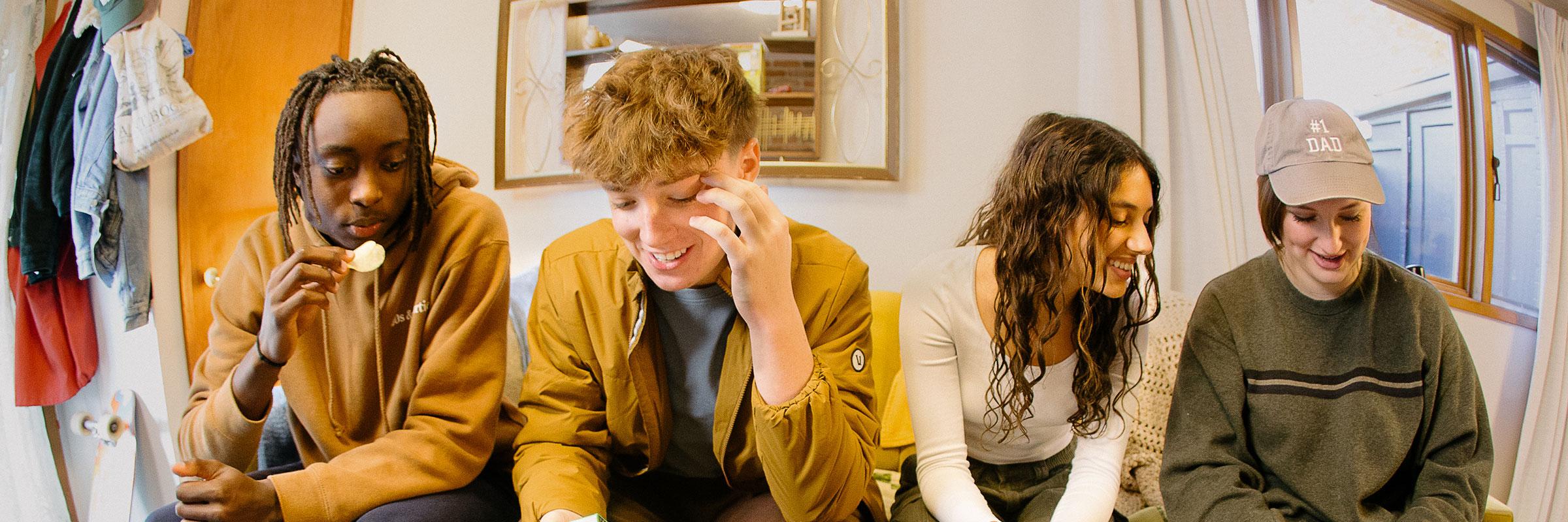 Close up image of four teenagers sitting together on a couch. 