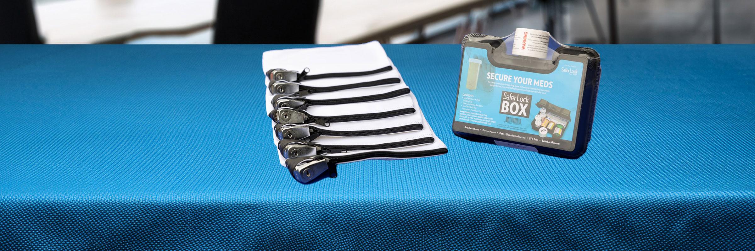 Table with bright blue tablecloth. Locking bag and locking box are on top of the table.